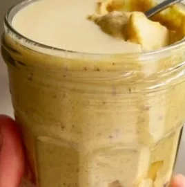 A bowl of blended peach oats topped with fresh peach slices and nuts.