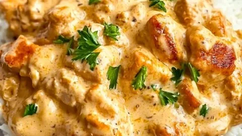 Creamy smothered chicken served over rice, garnished with herbs.