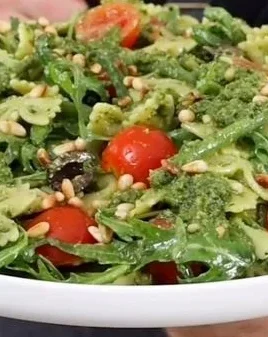 Colorful pesto pasta salad with vegetables and topped with pine nuts