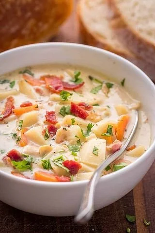 Delicious bowl of creamy clam chowder garnished with herbs and crackers