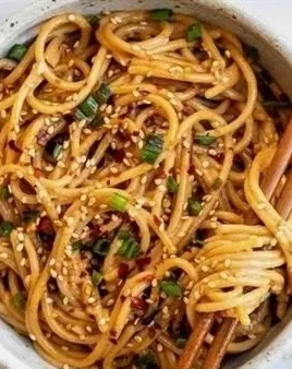 Delicious Garlic Sesame Noodles served in a bowl with sesame seeds and green onions.
