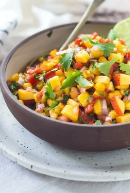 A bowl of fresh peach salsa with colorful ingredients like peaches, tomatoes, and cilantro.