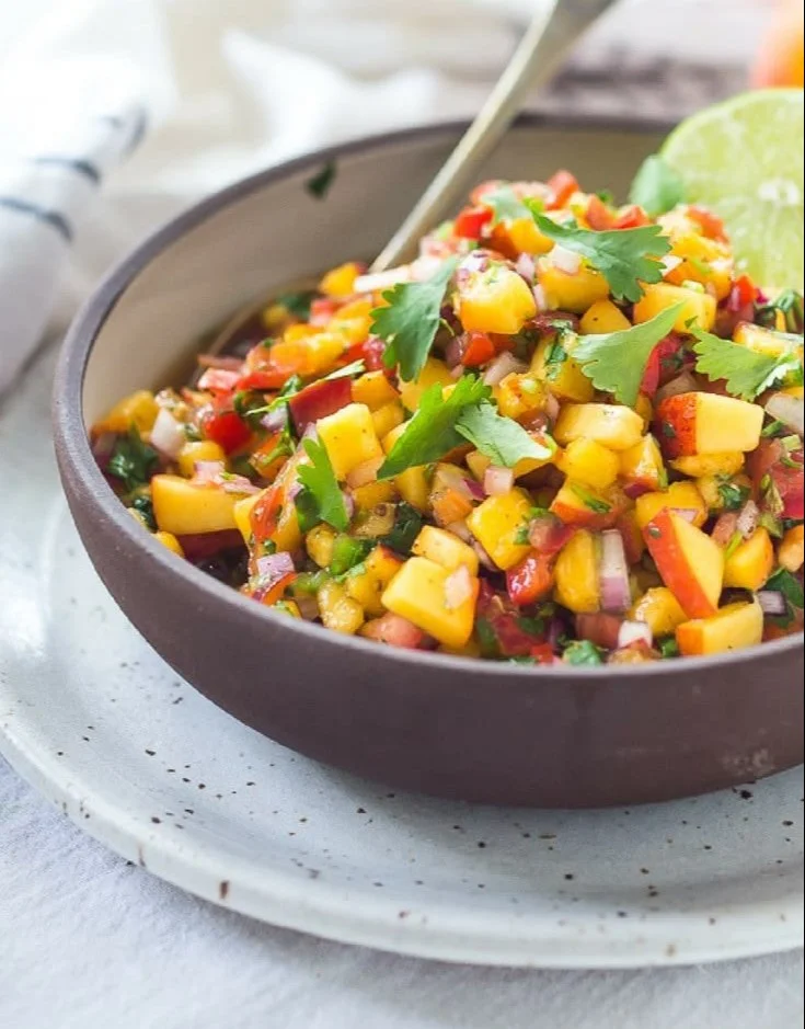 A bowl of fresh peach salsa with colorful ingredients like peaches, tomatoes, and cilantro.