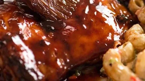 Succulent sticky grilled chicken on the barbecue, garnished with fresh herbs.