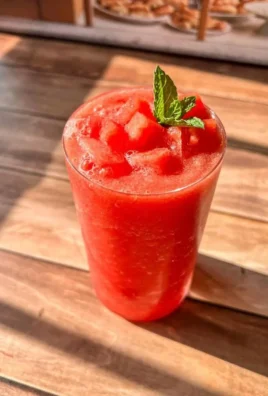 A vibrant watermelon slushie served in a glass with ice and mint garnish.